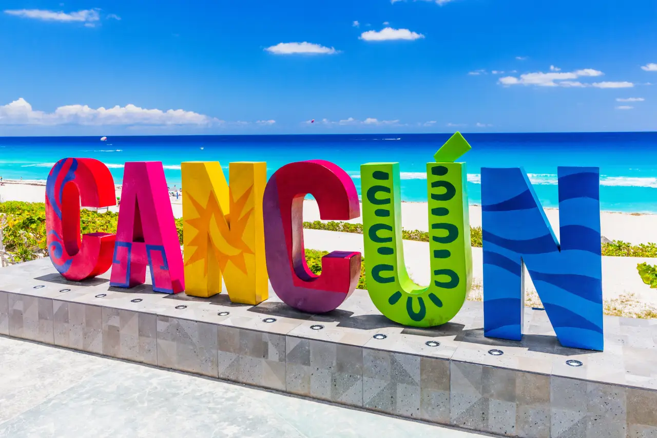 Colorful ‘Cancún’ sign with a bright blue ocean and sandy beach in the background.