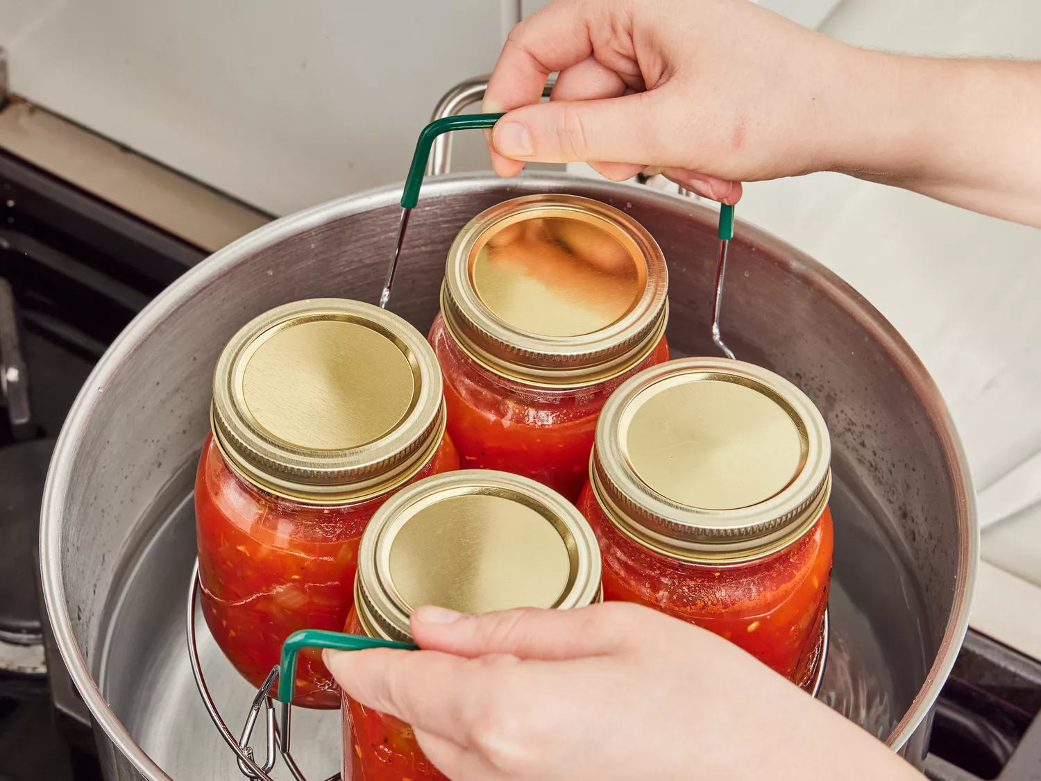 Jars of salsa being lowered into a half full stockpot.
