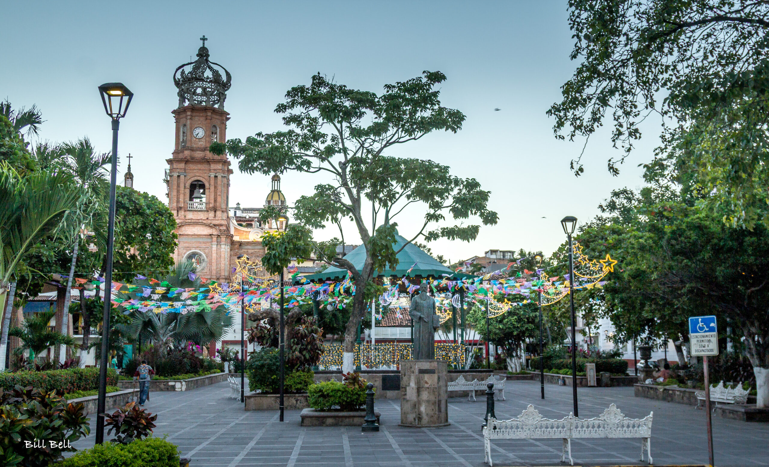 A decorated plaza in Puerto Vallarta, with benches, a gazebo and a crowned church tower.
